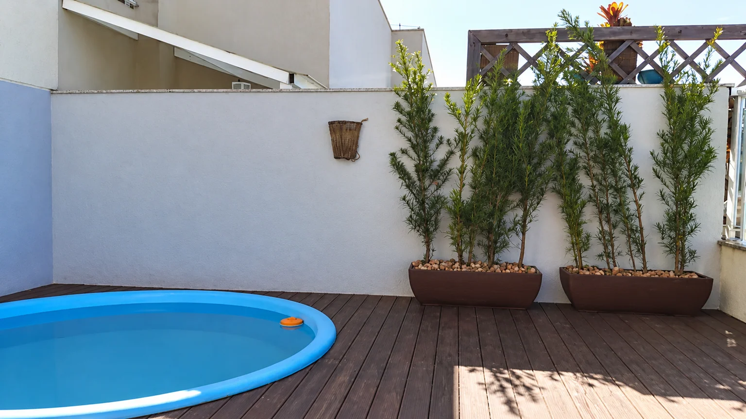 Área de lazer antes da intervenção, com muro branco, piscina e vasos sobre o deck.